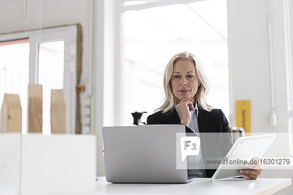 Female entrepreneur using laptop and digital tablet on desk in home office