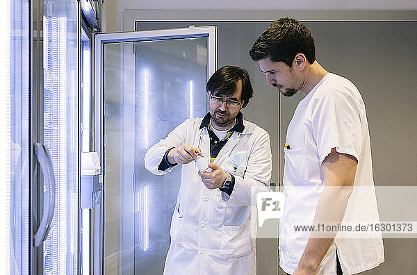 Männliche Apotheker bei der Suche nach Medikamenten vor einem beleuchteten Kühlschrank im Krankenhaus