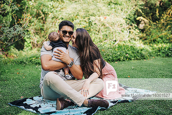 Cheerful family sitting on picnic blanket at park during weekend