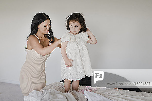 Lächelnde Mutter,  die ihre Tochter anzieht,  während sie im Schlafzimmer steht