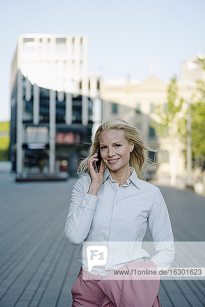 Lächelnde Unternehmerin  die im Finanzdistrikt mit einem Mobiltelefon spricht