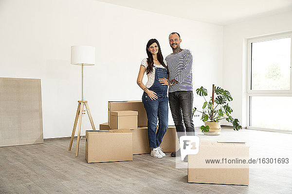 Happy couple standing by cardboard boxes and electric lamp in new unfurnished home