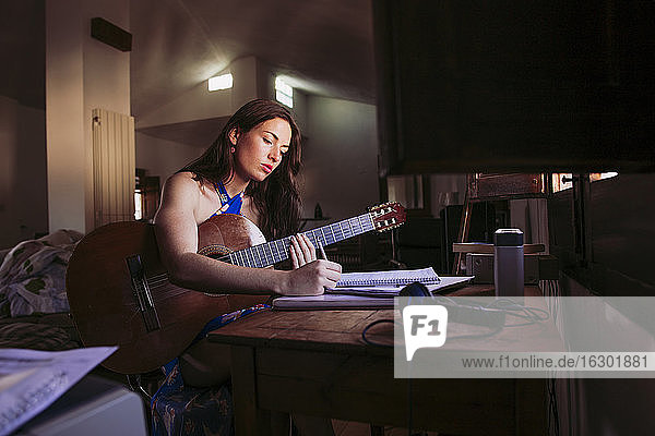 Junge Frau schreibt in ein Buch  während sie zu Hause Gitarre übt