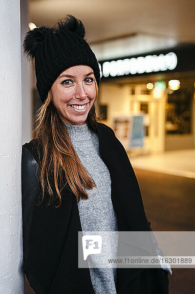 Smiling woman leaning on wall outdoors during winter
