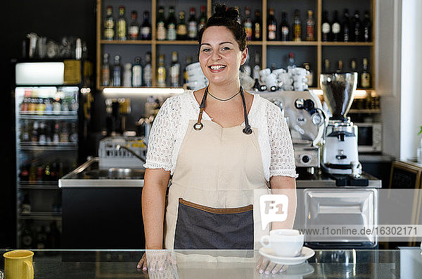 Lächelnde Besitzerin mit Kaffee auf dem Tresen eines Cafés