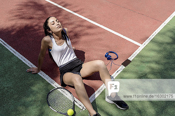 Tennisspielerin mit geschlossenen Augen  die sich auf dem Boden eines Sportplatzes entspannt