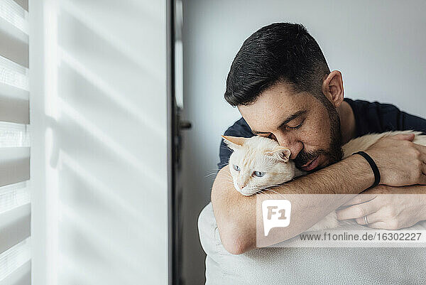 Mittlerer erwachsener Mann  der zu Hause sitzend eine Katze in die Arme nimmt