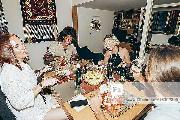 Cheerful friends eating pizza during party at home