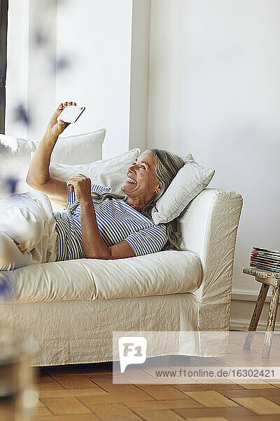 Frau benutzt Smartphone auf Sofa im Wohnzimmer