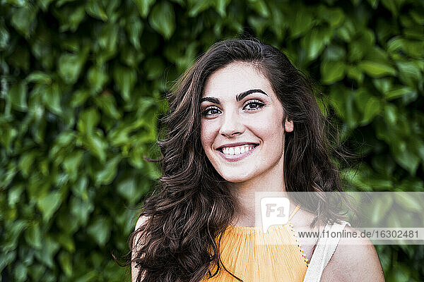 Lächelnde schöne junge Frau mit langen braunen Haaren  die vor Pflanzen steht