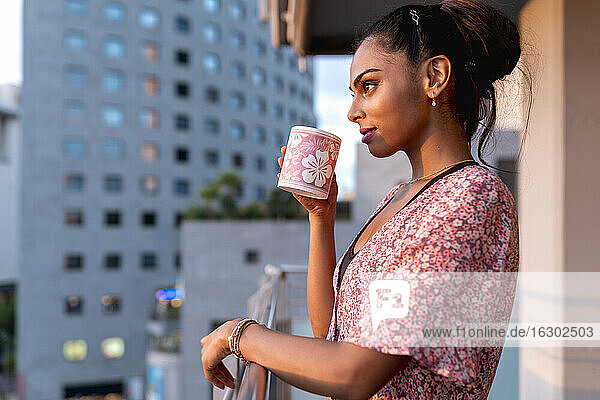 Schöne Frau steht auf dem Balkon und schlürft Kaffee bei Sonnenuntergang