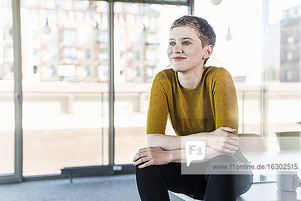 Lächelnde Geschäftsfrau sitzt auf dem Schreibtisch im Büro