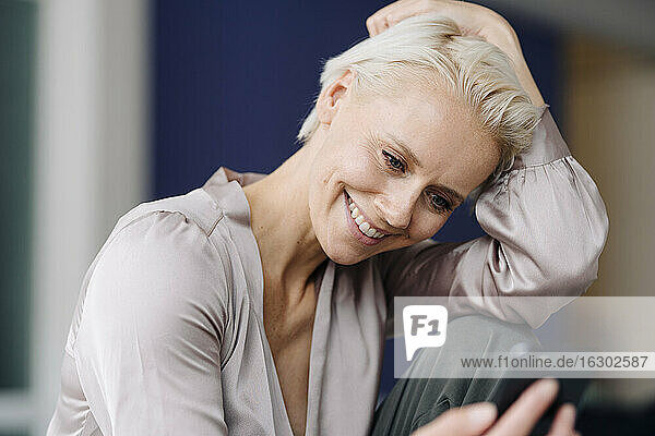 Nahaufnahme einer lächelnden Geschäftsfrau  die ein Mobiltelefon benutzt  während sie im Büro sitzt