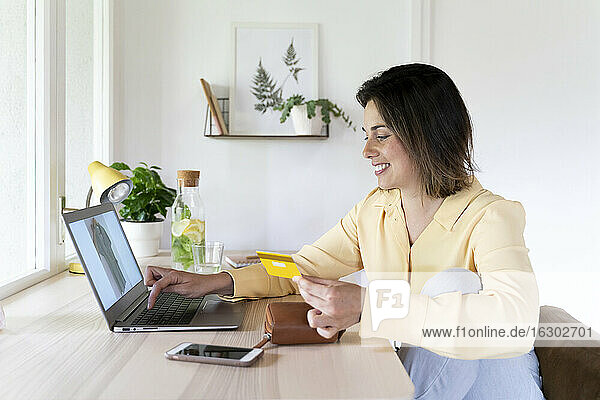 Happy beautiful young woman using laptop for online shopping at home