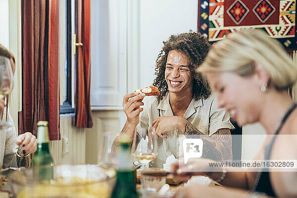 Glücklicher Mann beim Essen  während er mit Freunden zu Hause eine Party feiert