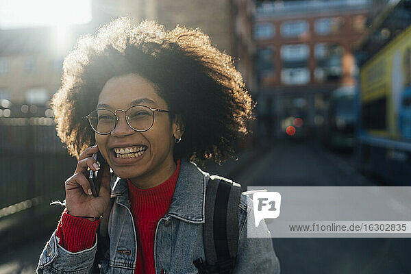 Close-up of cheerful young woman with curly hair talking over smart phone in city