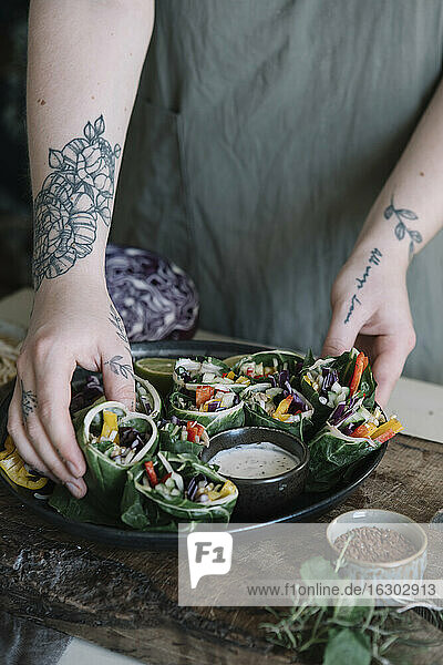 Young woman preparing vegan roll with vegetables and yoghurt sauce