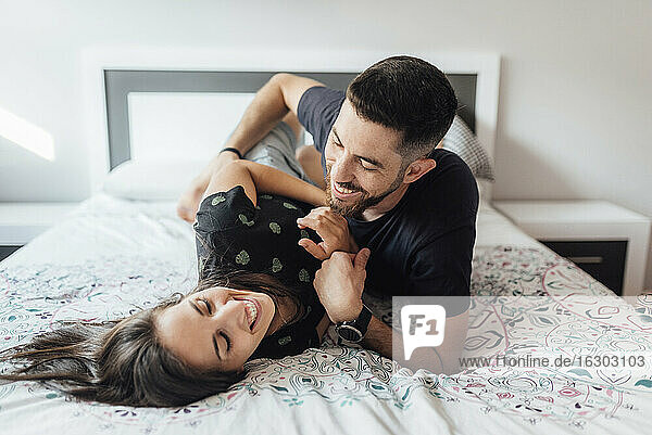 Smiling couple playing on bed in bedroom at home
