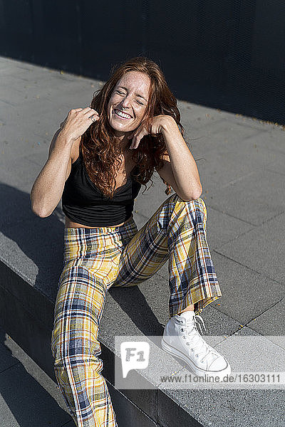 Fröhliche Frau sitzt auf dem Bürgersteig in der Stadt an einem sonnigen Tag