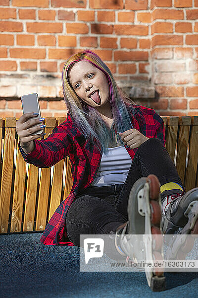 Junge Frau mit gefärbten Haaren und Rollschuhen macht ein Selfie und streckt die Zunge heraus