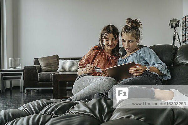 Friends doing online shopping over digital tablet while relaxing on sofa at home