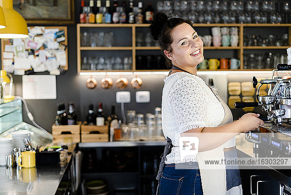 Lächelnde weibliche Barista  die bei der Arbeit in einem Café an der Kaffeemaschine steht