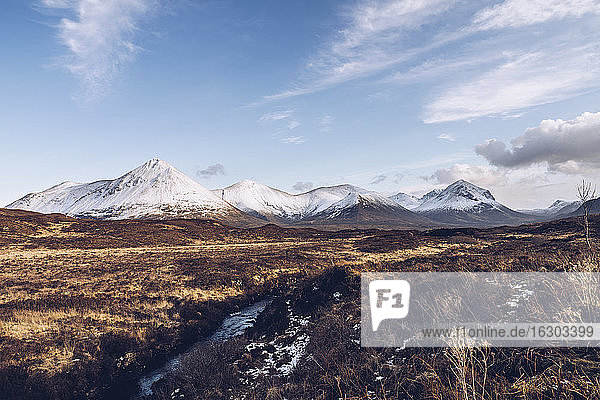 UK  Scotland  River flowing on Isle of Skye in winter with snowcapped mountains in background