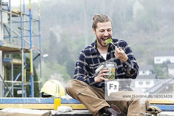 Construction worker eating salad while sitting outdoors at construction site