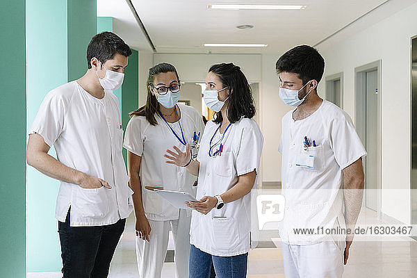 Ärzte  die chirurgische Masken tragen  diskutieren über ein digitales Tablet  während sie im Krankenhaus stehen