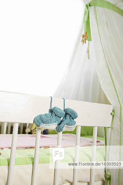 Blaue Babyschuhe hängen am Kinderbett