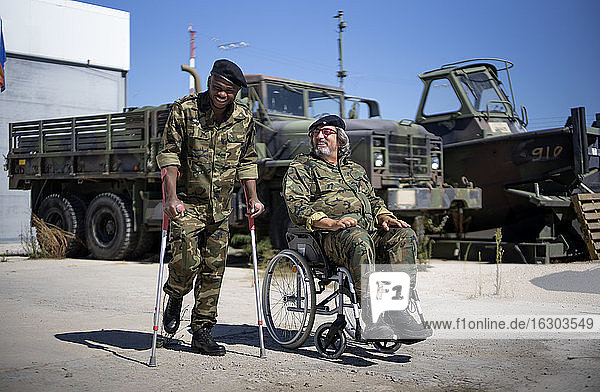 Junger Militäroffizier mit Krücken lächelt  während sein Kollege an einem sonnigen Tag im Rollstuhl sitzt