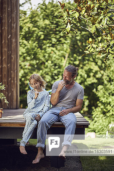 Vater und Tochter putzen sich die Zähne  während sie vor dem Haus im Hof sitzen