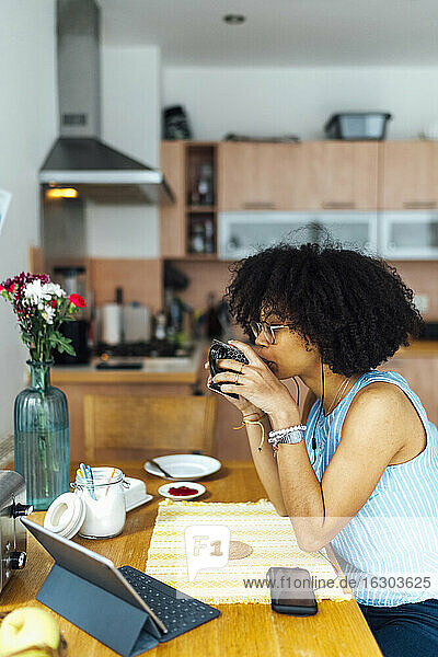 Geschäftsfrau mit lockigem Haar trinkt Kaffee  während sie am Schreibtisch im Heimbüro sitzt