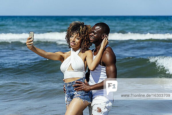 Junge Frau  die ein Selfie mit ihrem Freund macht  während sie im Meer steht