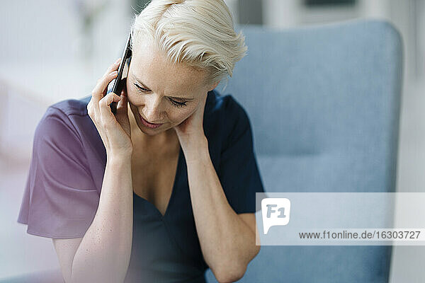 Nahaufnahme einer Geschäftsfrau  die über ein Smartphone spricht und nach unten schaut  während sie im Büro sitzt