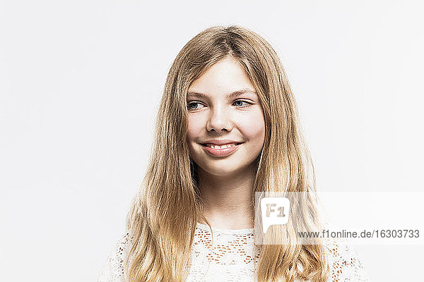 Close-up of smiling girl with blond hair looking away against white background