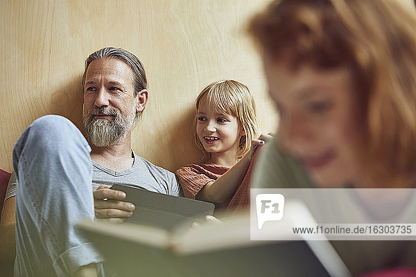 Frau liest ein Buch  während Vater und Tochter zu Hause im Hintergrund wegschauen