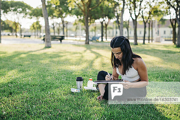 Young woman doing watercolor painting in book while sitting in park