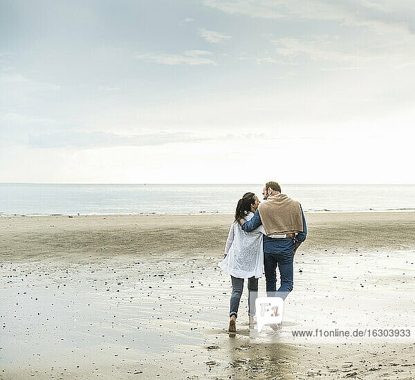 Älteres Paar mit Armen um genießen Wochenende am Strand gegen bewölkten Himmel
