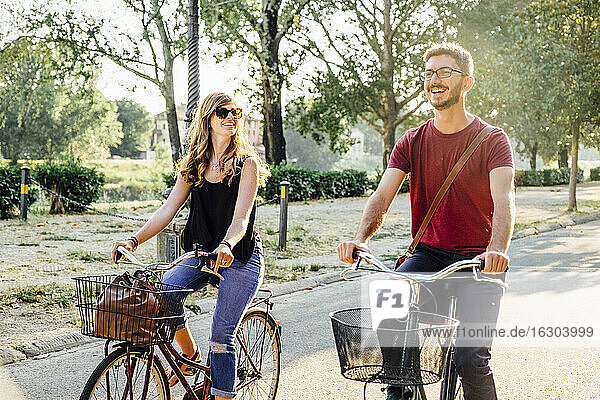 Happy couple riding bicycles on road in park during weekend