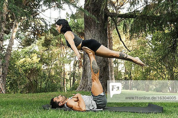 Mann balanciert seine Freundin auf den Beinen  während er im Park Acroyoga übt