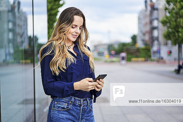 Frau schreibt Textnachrichten über ihr Mobiltelefon  während sie auf einem Fußweg in der Stadt steht