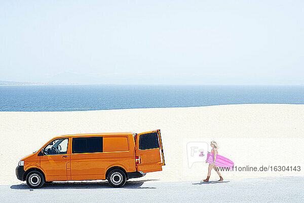Junge Frau hält Surfbrett beim Spaziergang am Strand an einem sonnigen Tag