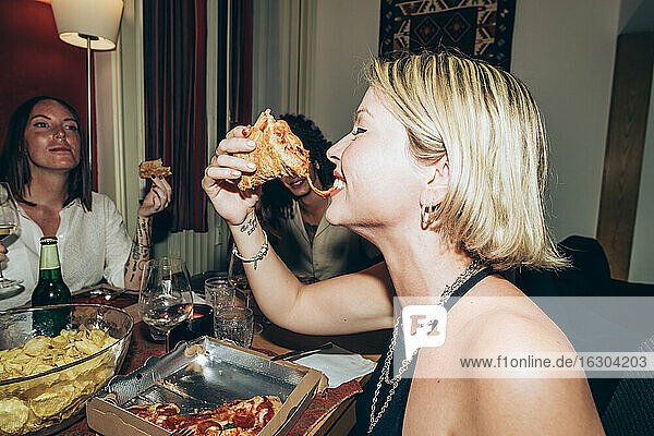 Smiling young woman eating pizza during party