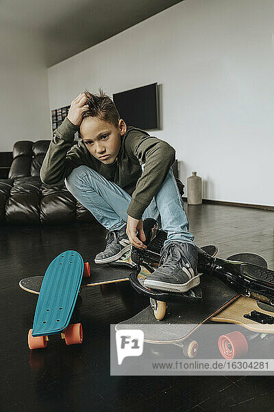Verwirrter Junge mit Skateboards  der zu Hause auf dem Boden hockt