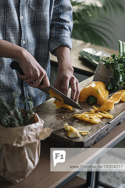 Mittelteil eines jungen Mannes  der gelbe Paprika auf einem Brett in der Küche schneidet