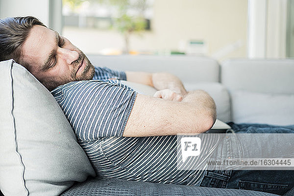 Man with laptop sleeping on sofa in living room