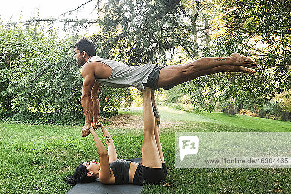 Weibliche Athletin balanciert ihren Freund auf den Beinen  während sie sich im Park an den Händen hält