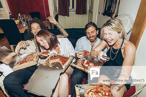 Fröhliche Freunde sehen fern  während sie auf einer Party zu Hause Pizza essen