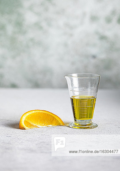 Slice of orange and cup of olive oil for making vinaigrette
